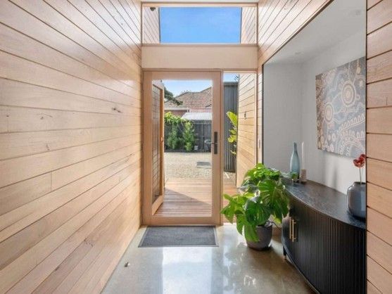 Bright entry hallway with wood-paneled wall, glass door, potted plant, and black console table. Bright entry hallway with wood-paneled wall, glass door, potted plant, and black console table.