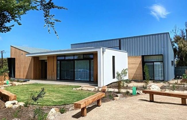 Modern single-story house with wood and metal exterior, large windows, and a small front yard under a blue sky Modern single-story house with wood and metal exterior, large windows, and a small front yard under a blue sky