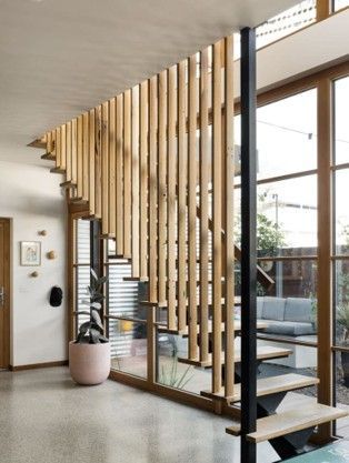 Modern interior with a wooden slatted staircase and black railing beside large windows. Modern interior with a wooden slatted staircase and black railing beside large windows.