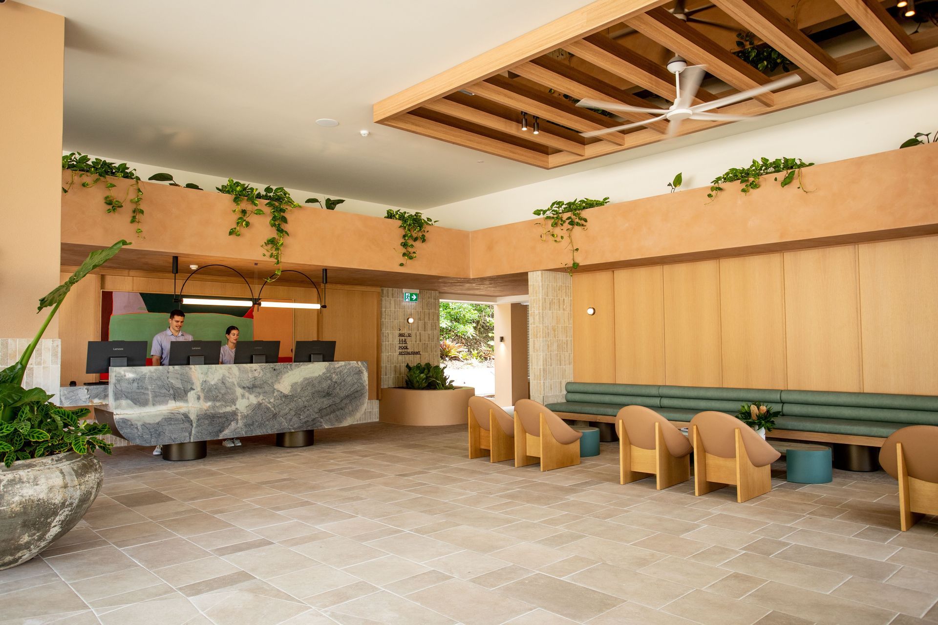 Modern restaurant interior with wood accents, green banquette seating, and a stone host counter