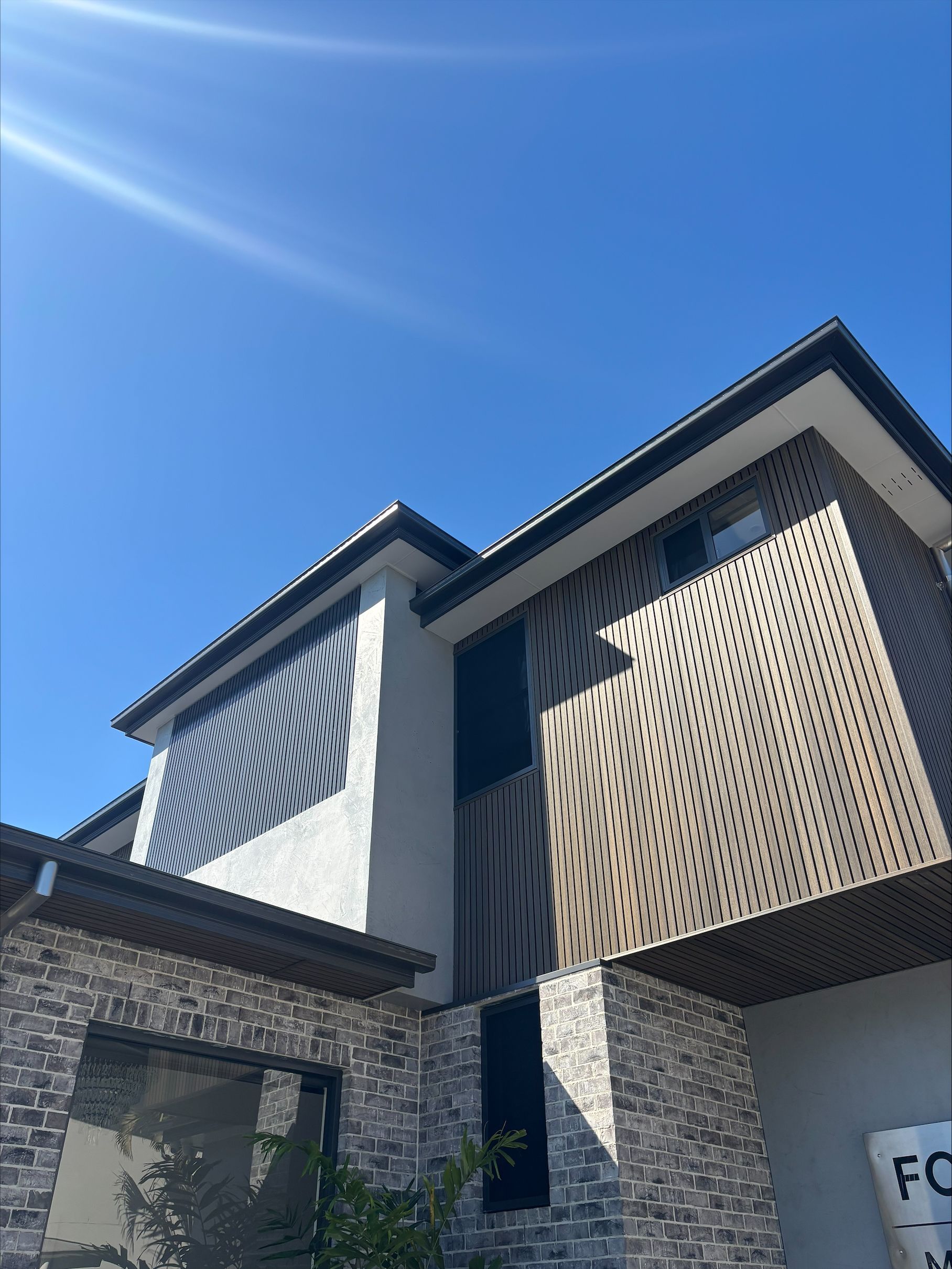 Modern house exterior with stone facade, beige lattice panels, and blue sky overhead