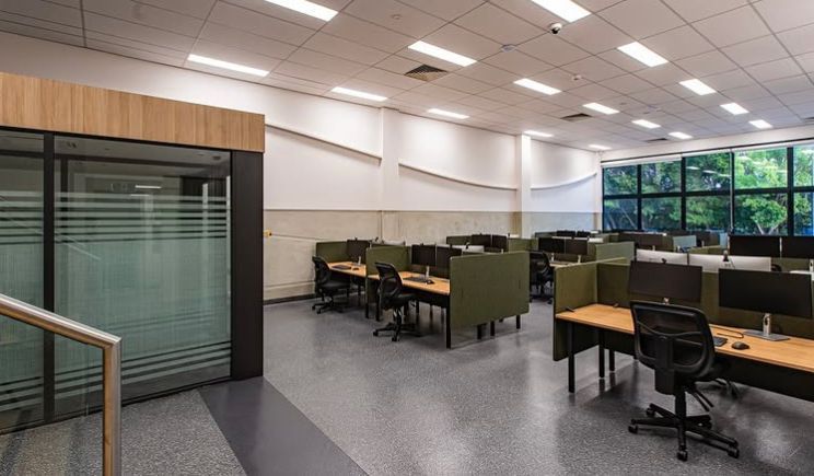 Modern office meeting area with desks, chairs, and large windows overlooking trees
