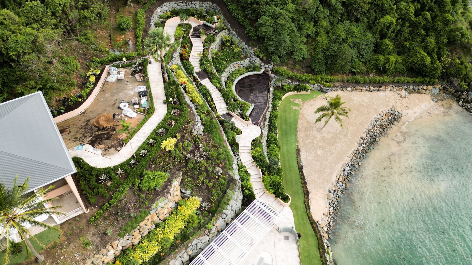 Aerial view of a lush seaside resort path beside a sandy beach and clear water