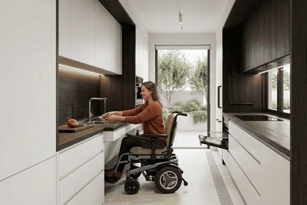 Person in wheelchair using a sink in a modern kitchen with open doorway to a garden