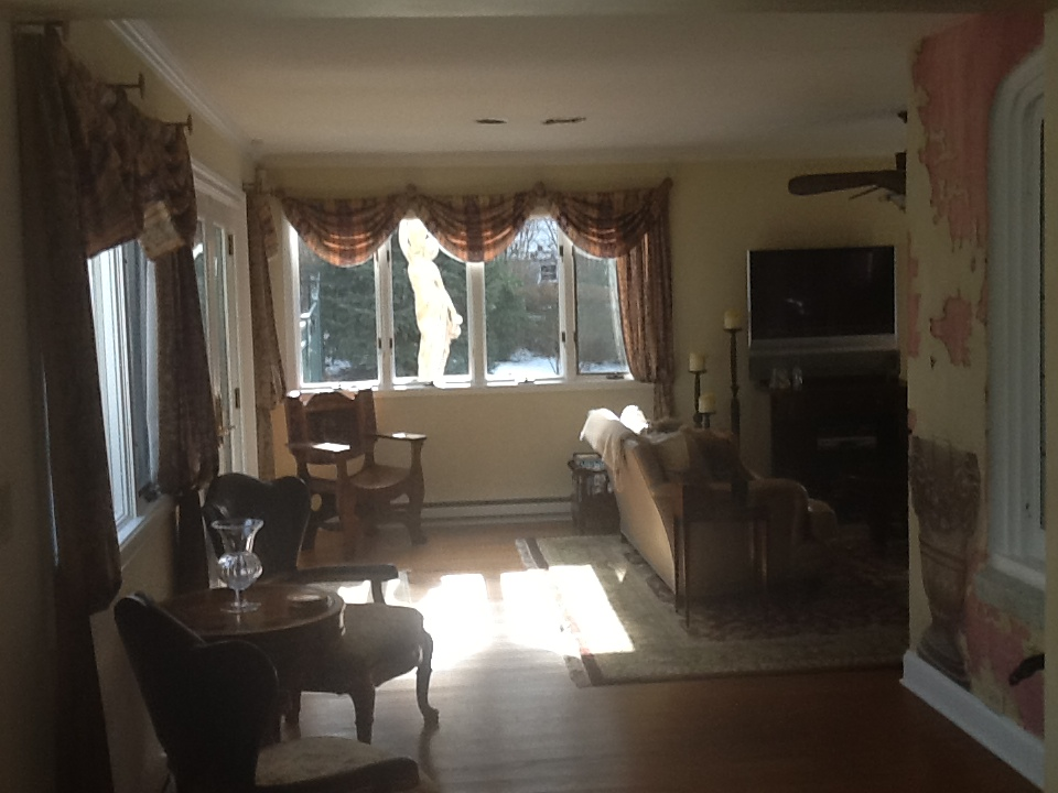 Sunlit living room with large windows, chairs, sofa, TV, and patterned drapes
