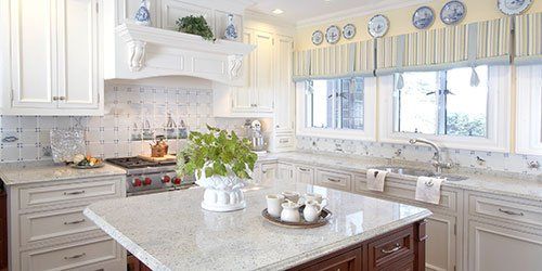 Bright white kitchen with marble island, farmhouse sink, blue accents, and large sunlit windows