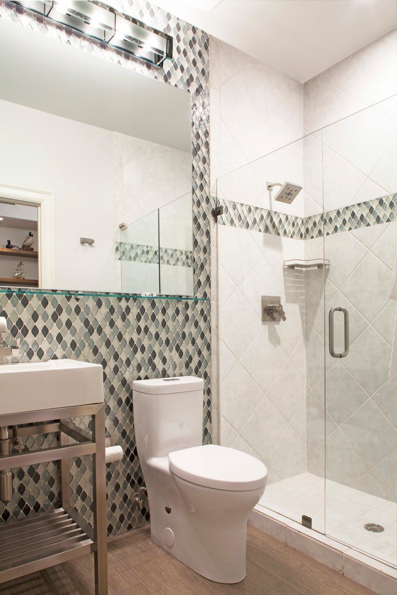 Modern tiled bathroom with toilet, sink, and walk-in shower with glass door