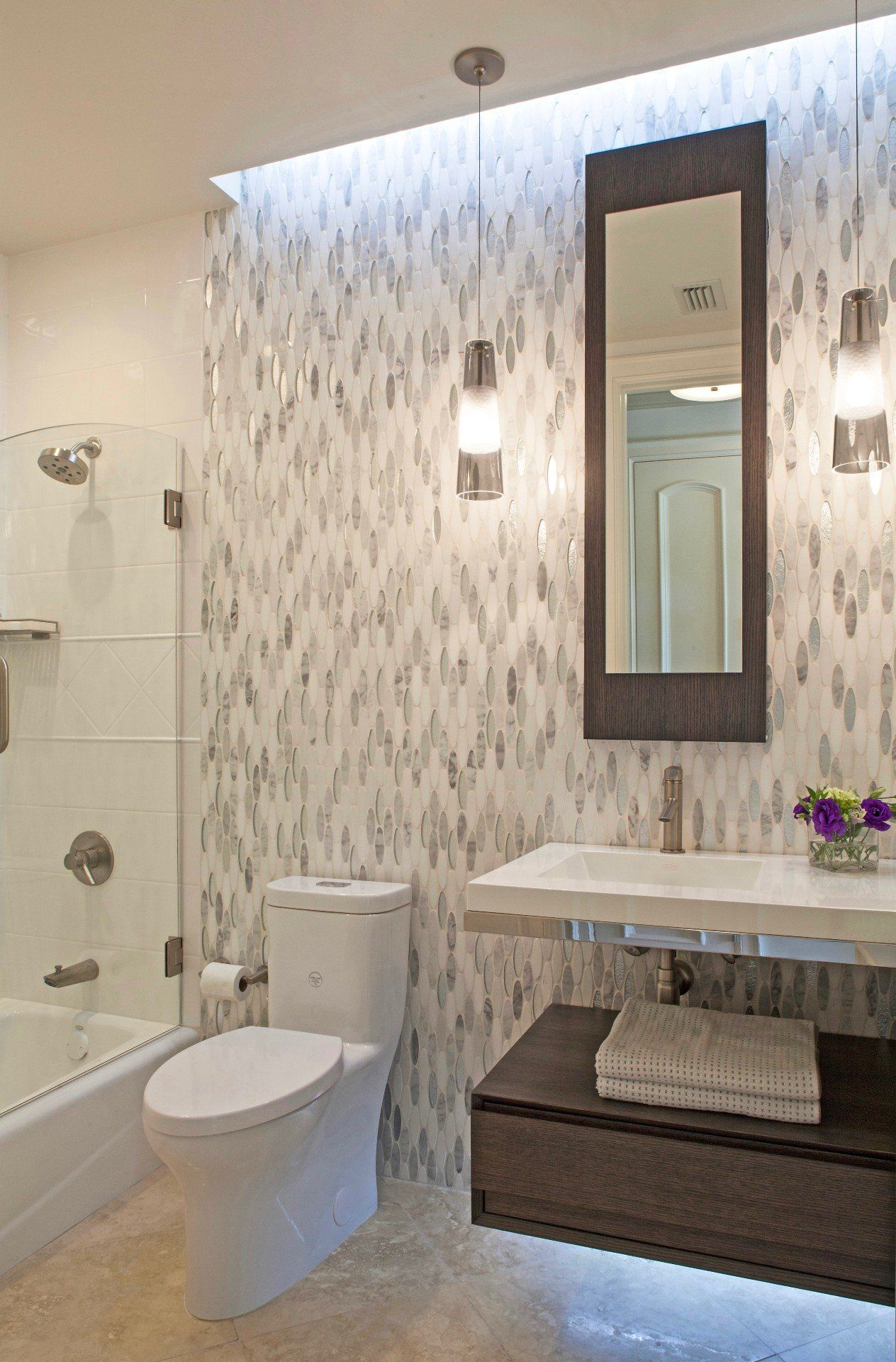 Modern bathroom with walk-in shower, toilet, vanity, mirror, and wall sconces