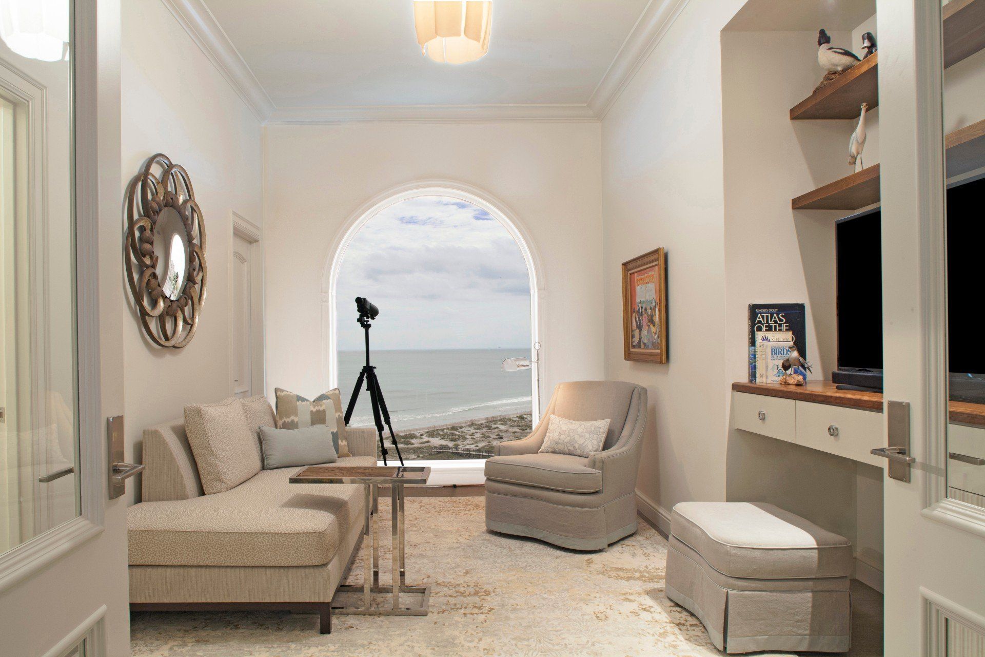 Cozy neutral-toned sitting room with arched window, telescope, and ocean view