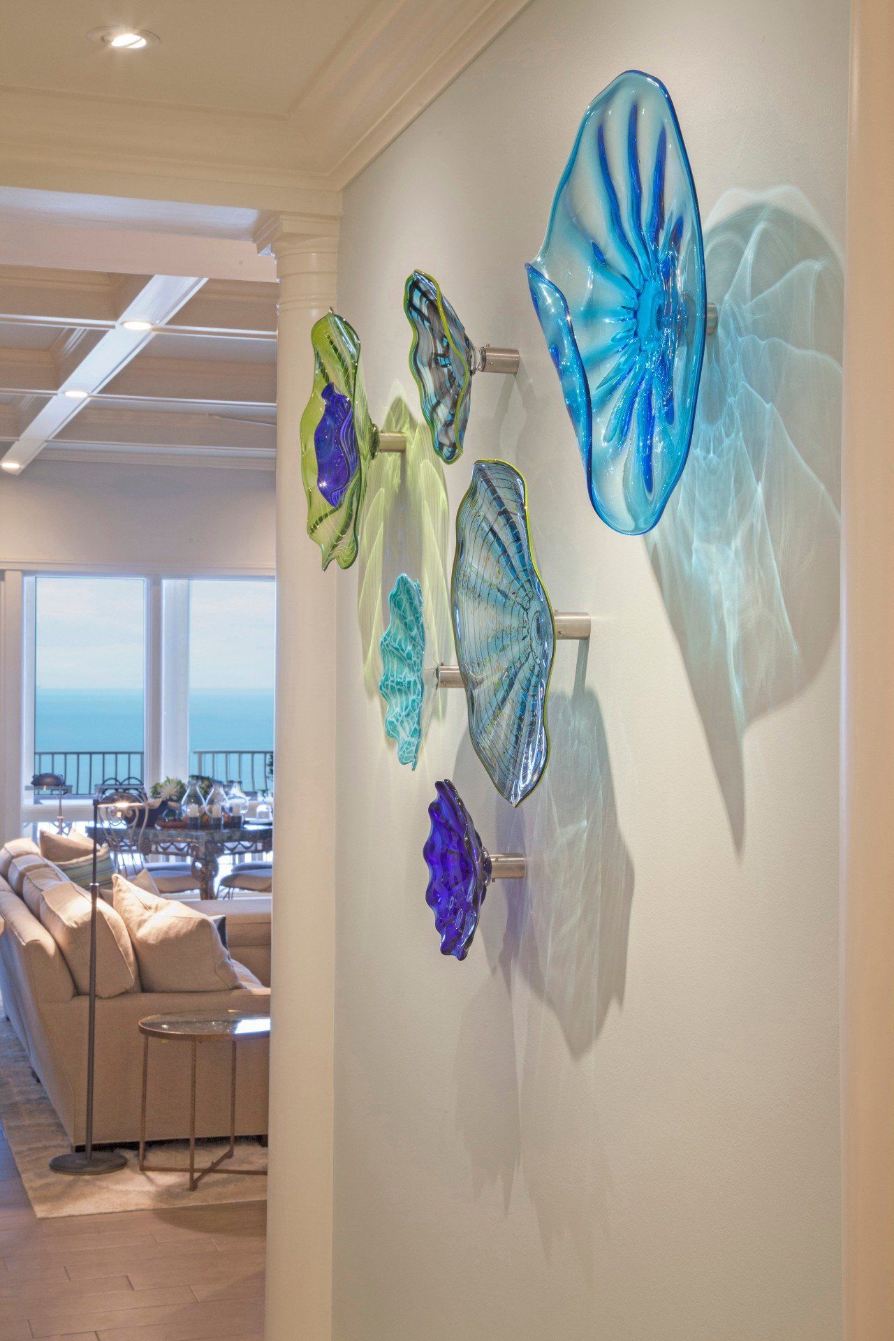 Colorful glass wall art in a bright hallway overlooking a dining room and ocean view