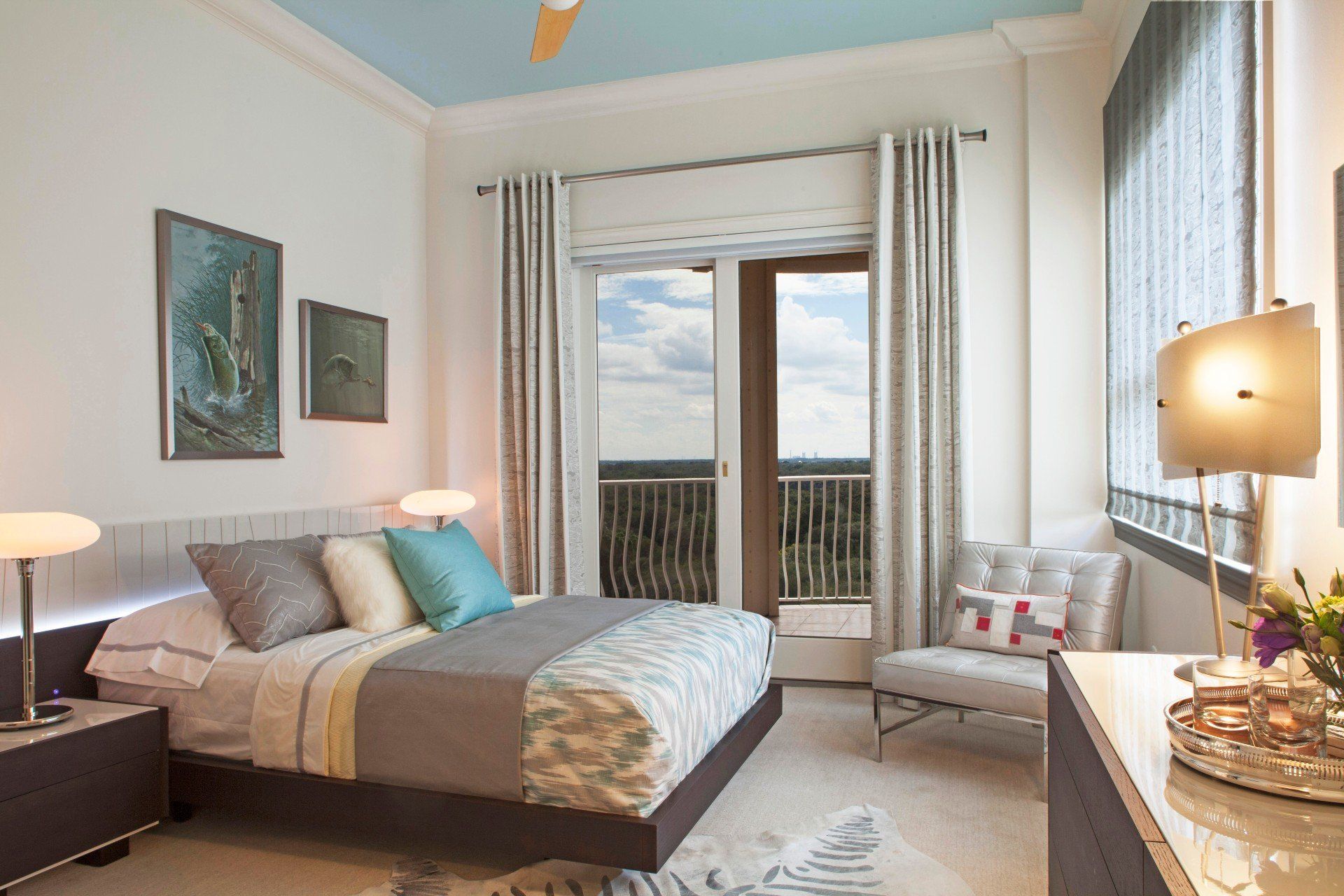 Bright bedroom with a bed, bedside lamps, artwork, and sliding doors to a balcony.