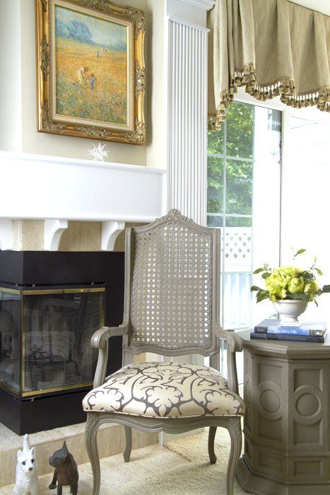 Elegant living room with fireplace, ornate chair, side table, and bright window with draped curtains