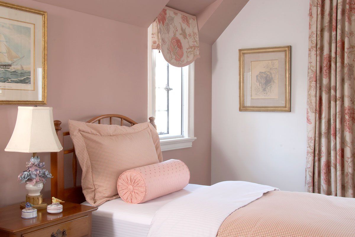 Pink bedroom with a neatly made bed, floral curtains, and framed wall art