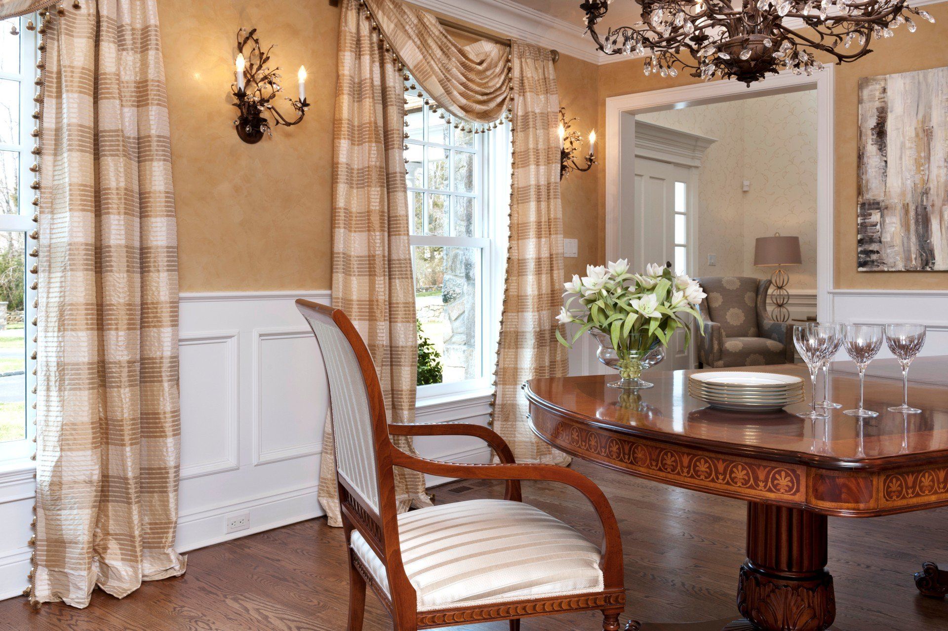 Elegant dining room with a wooden table, upholstered chair, chandelier, and cream plaid curtains by a bright window