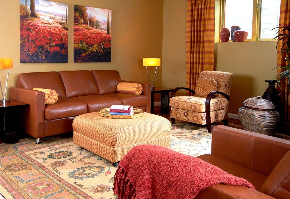 Cozy living room with brown leather sofa, patterned chairs, ottoman, and warm autumn artwork and decor