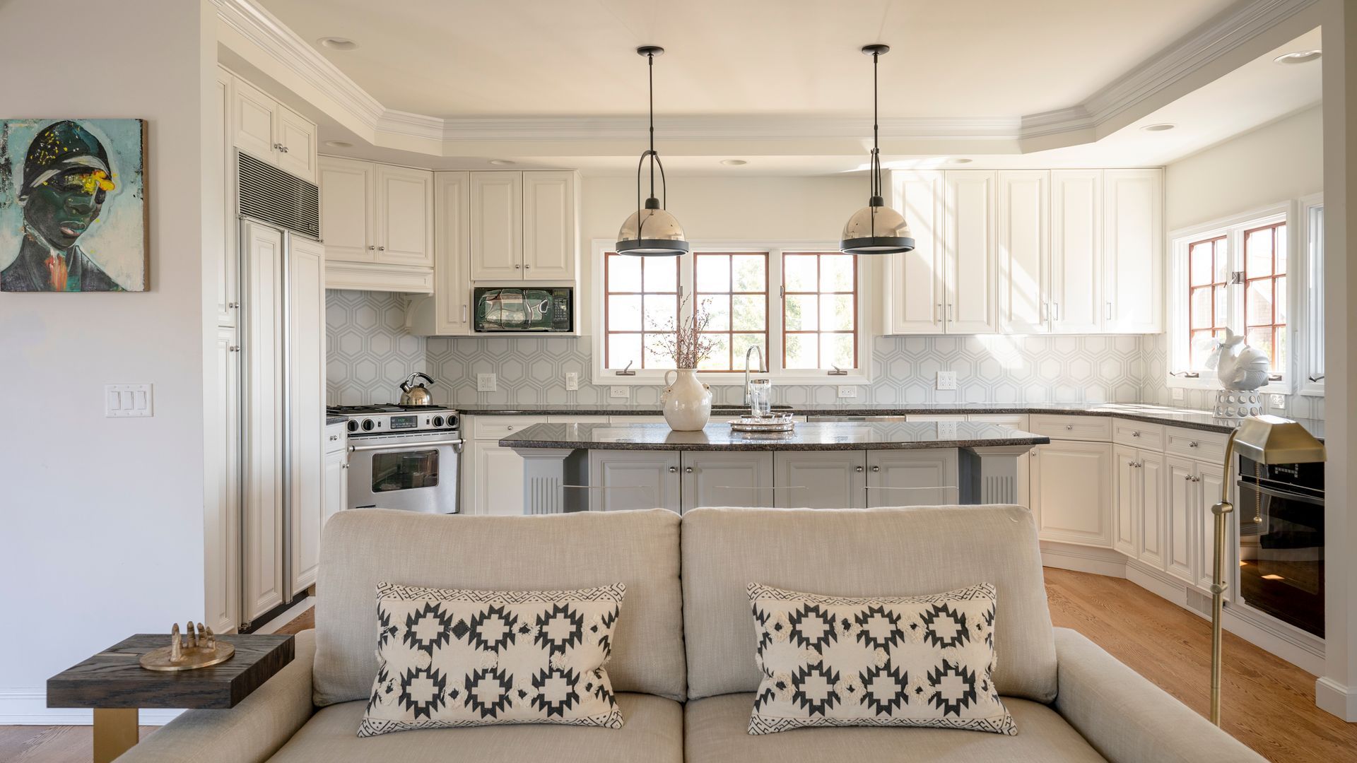 Bright white kitchen with island and pendant lights, viewed from a beige sofa in an open living space