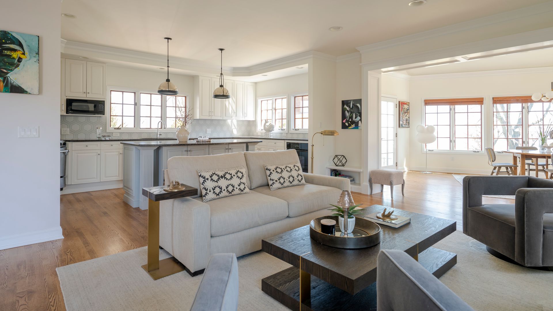 Bright open living room with gray sofa, coffee table, kitchen island, and large windows