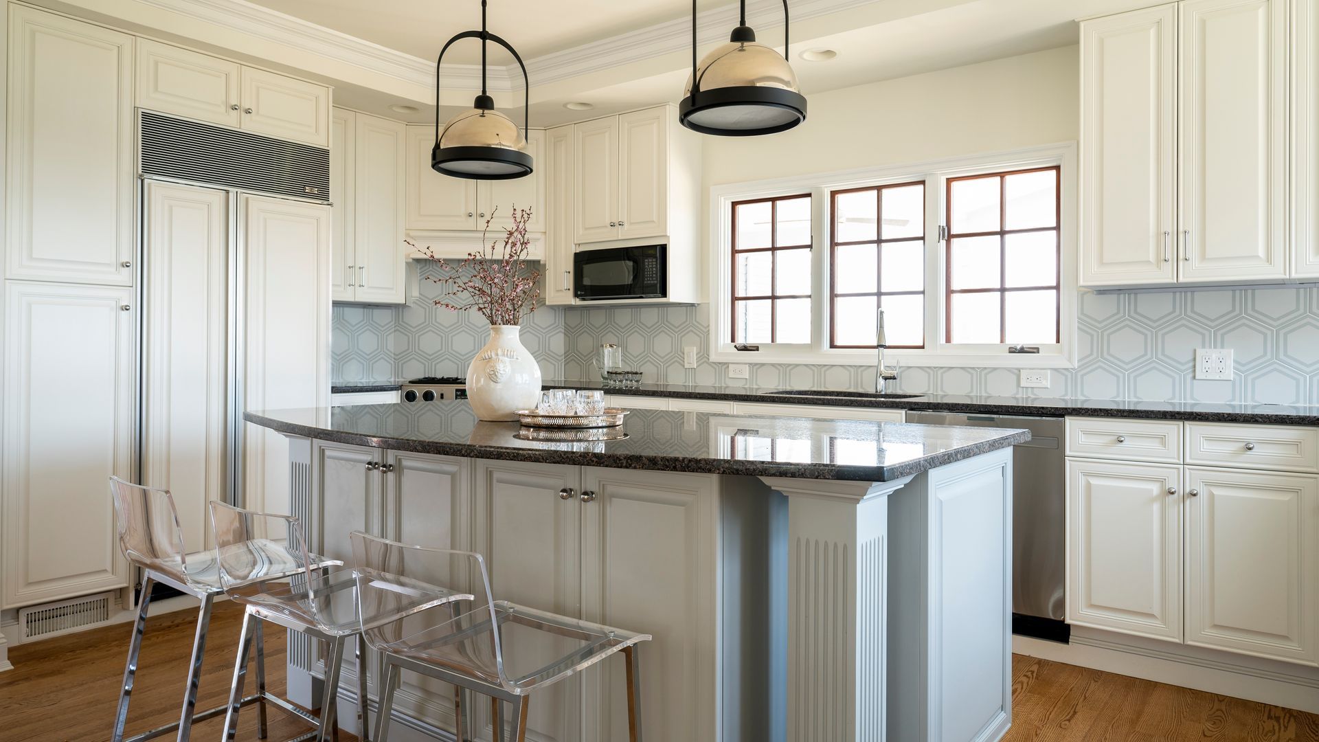 Bright modern kitchen with white cabinets, stainless island, pendant lights, and a window over the sink