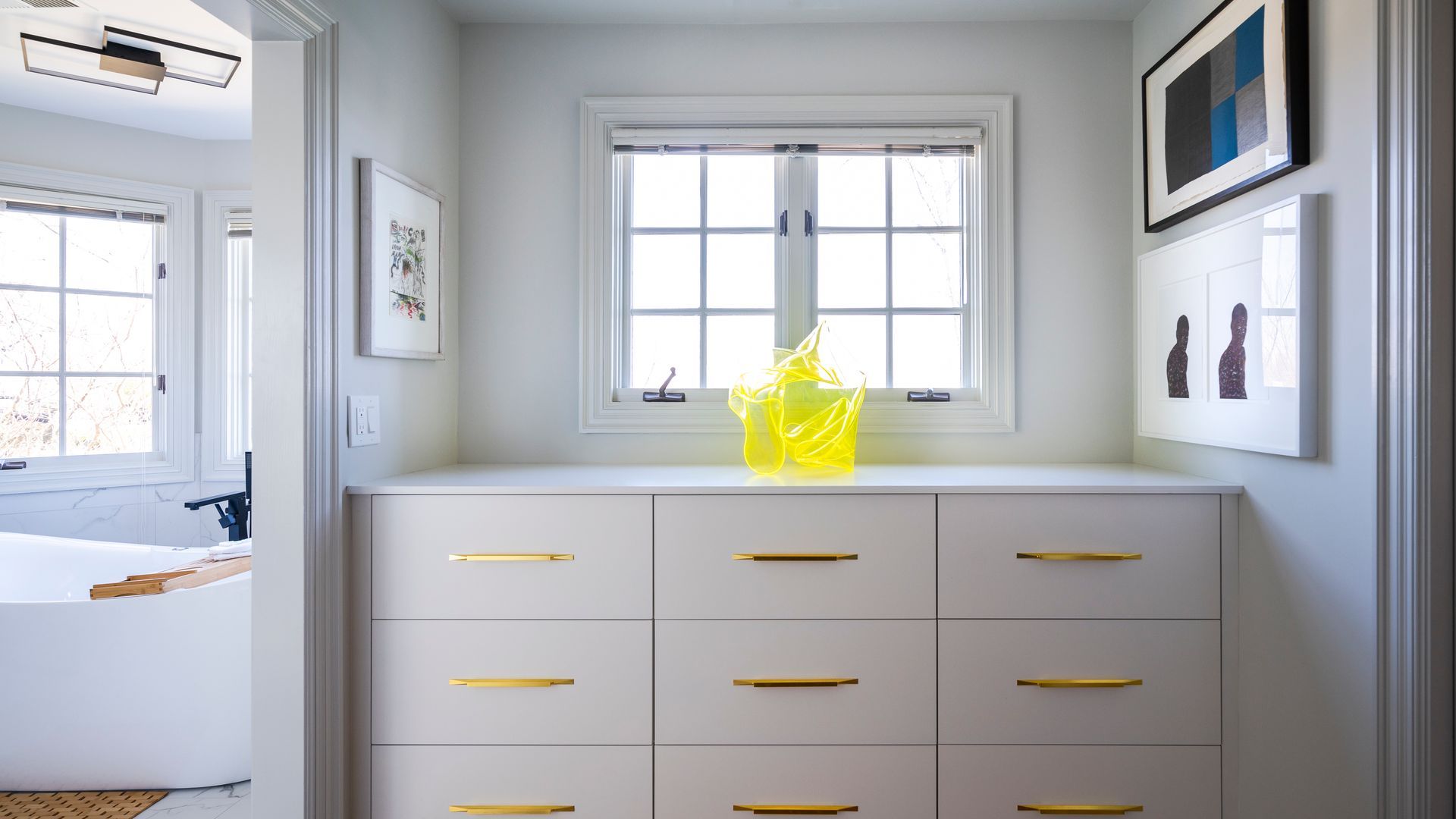 Bright room with white dresser, yellow vase, window, and framed wall art