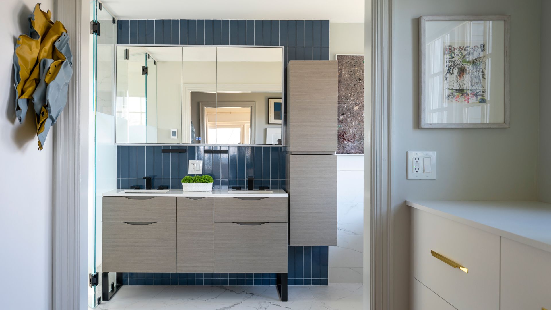 Modern bathroom vanity with mirror, light wood cabinets, dark tiles, and a framed wall print