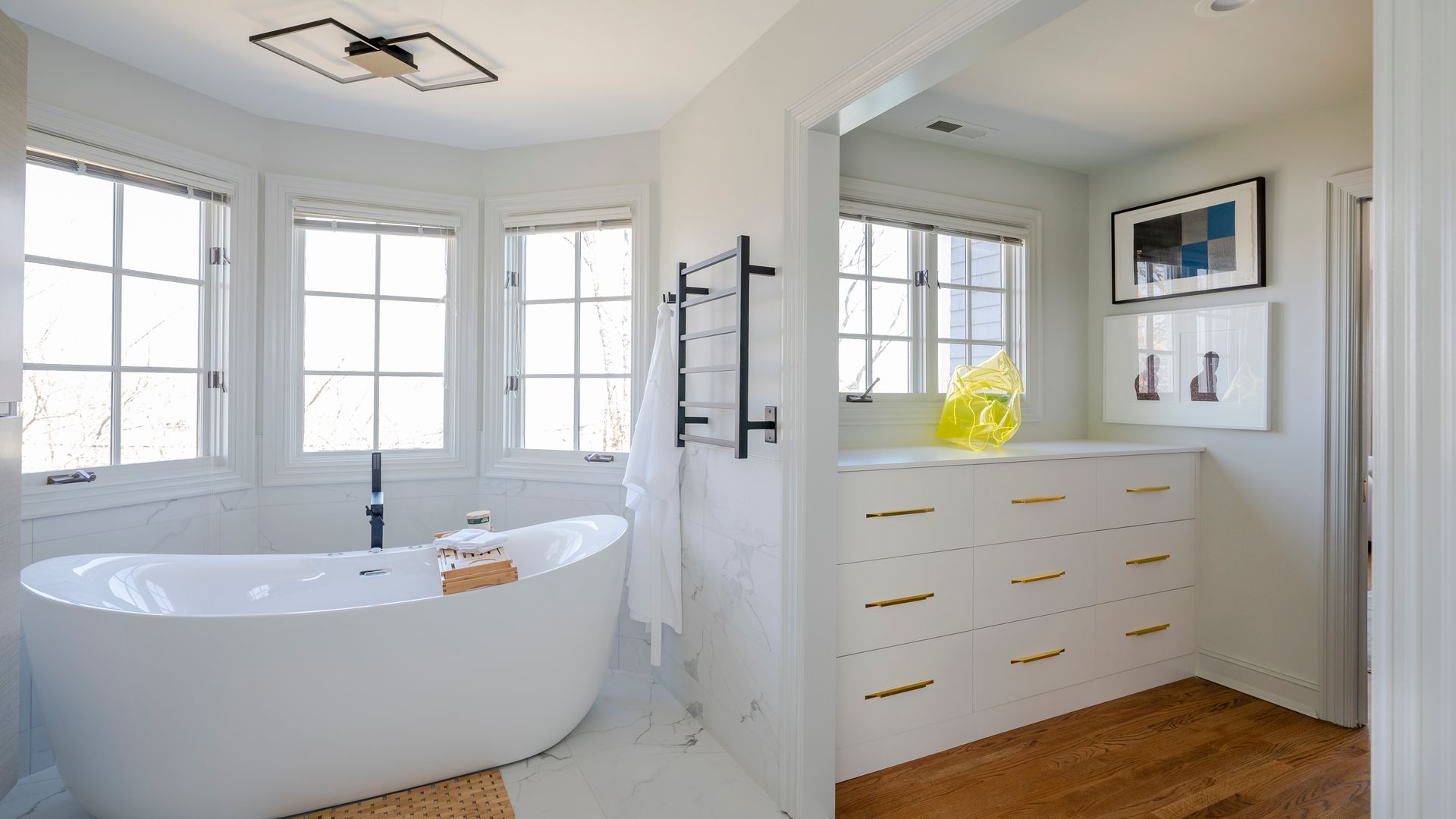 Bright white bathroom with a freestanding tub, vanity, and large windows