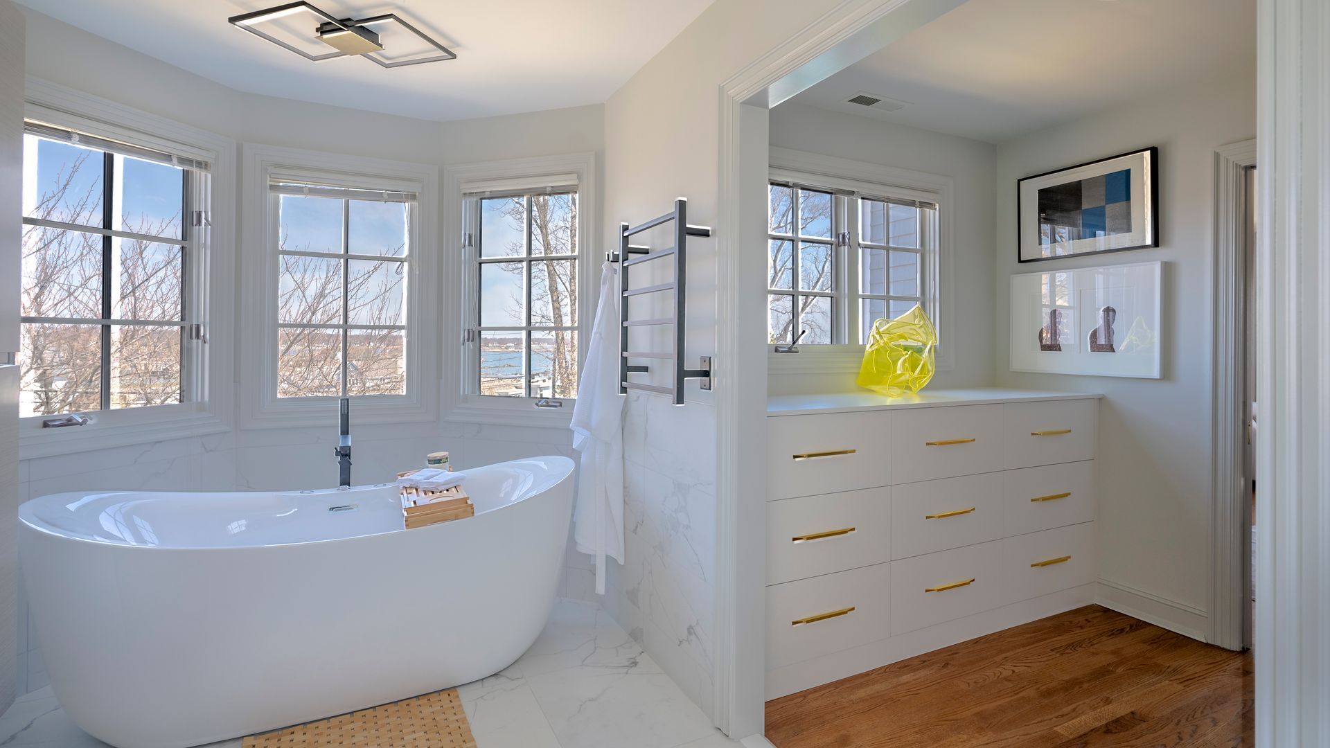 Bright bathroom with a freestanding tub, large windows, and a white vanity with gold handles.