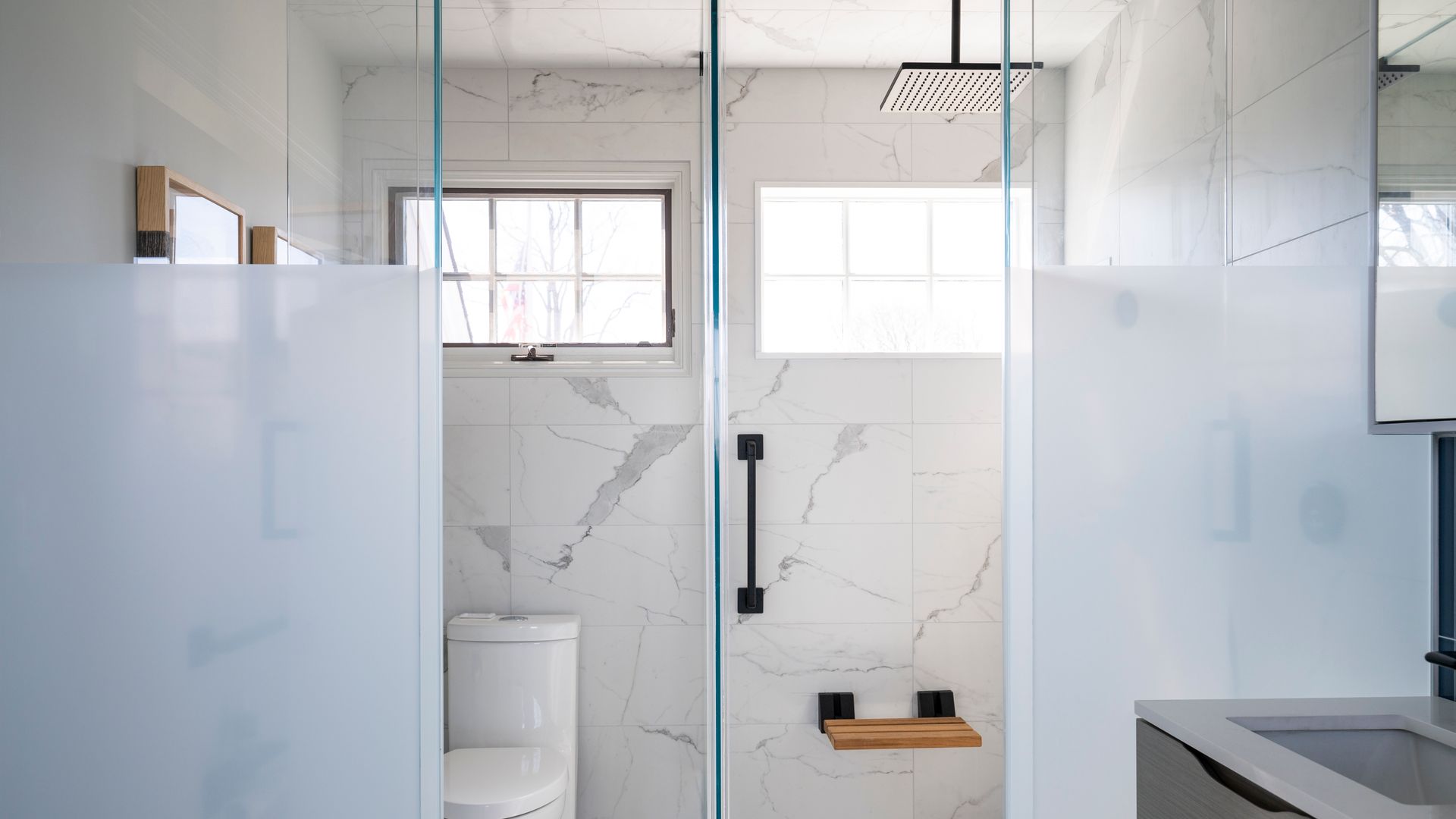 Modern bathroom with frosted glass partitions, tiled shower, windows, and a white toilet