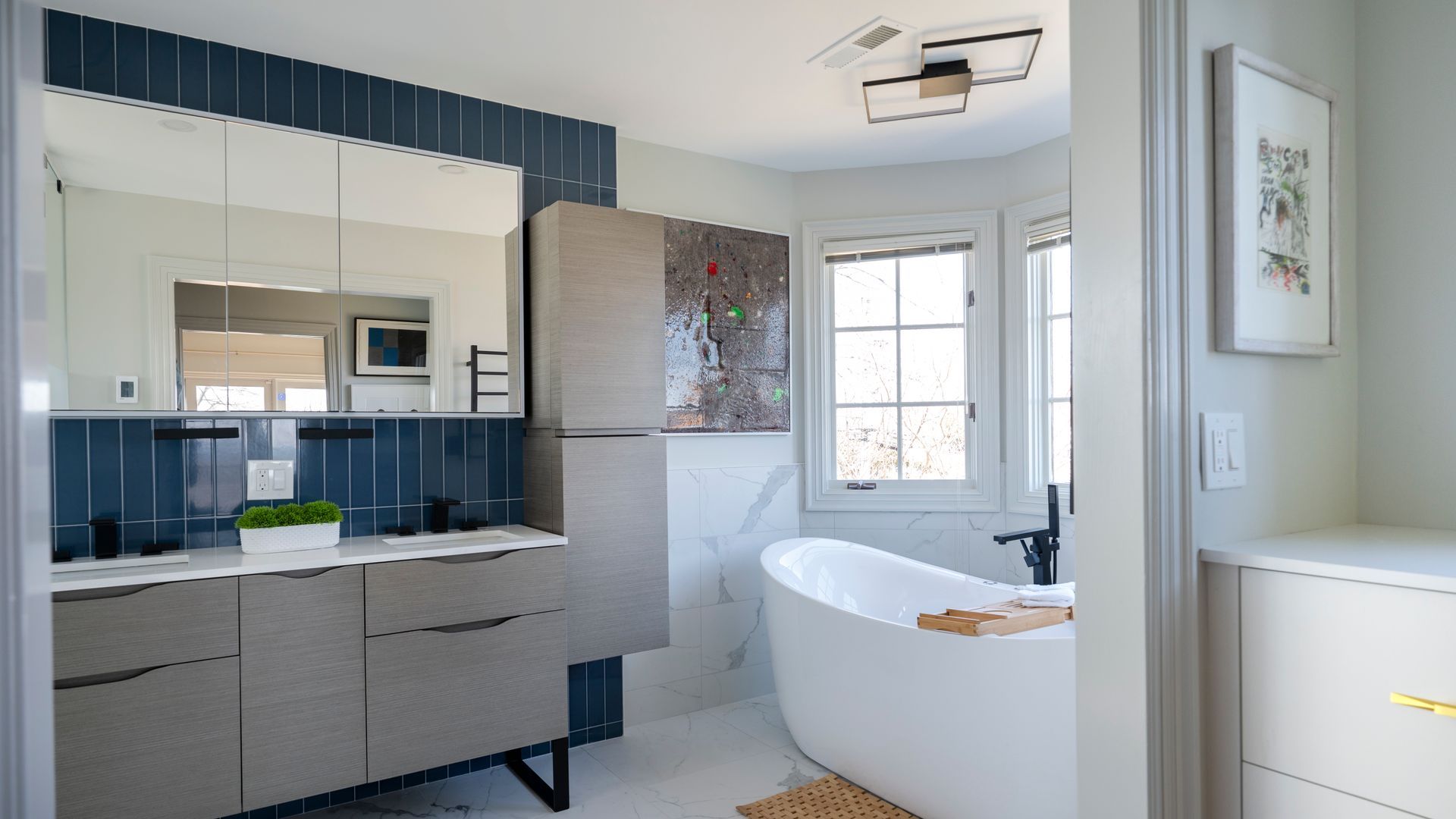 Bright modern bathroom with vanity, large mirror, white tub, and window light