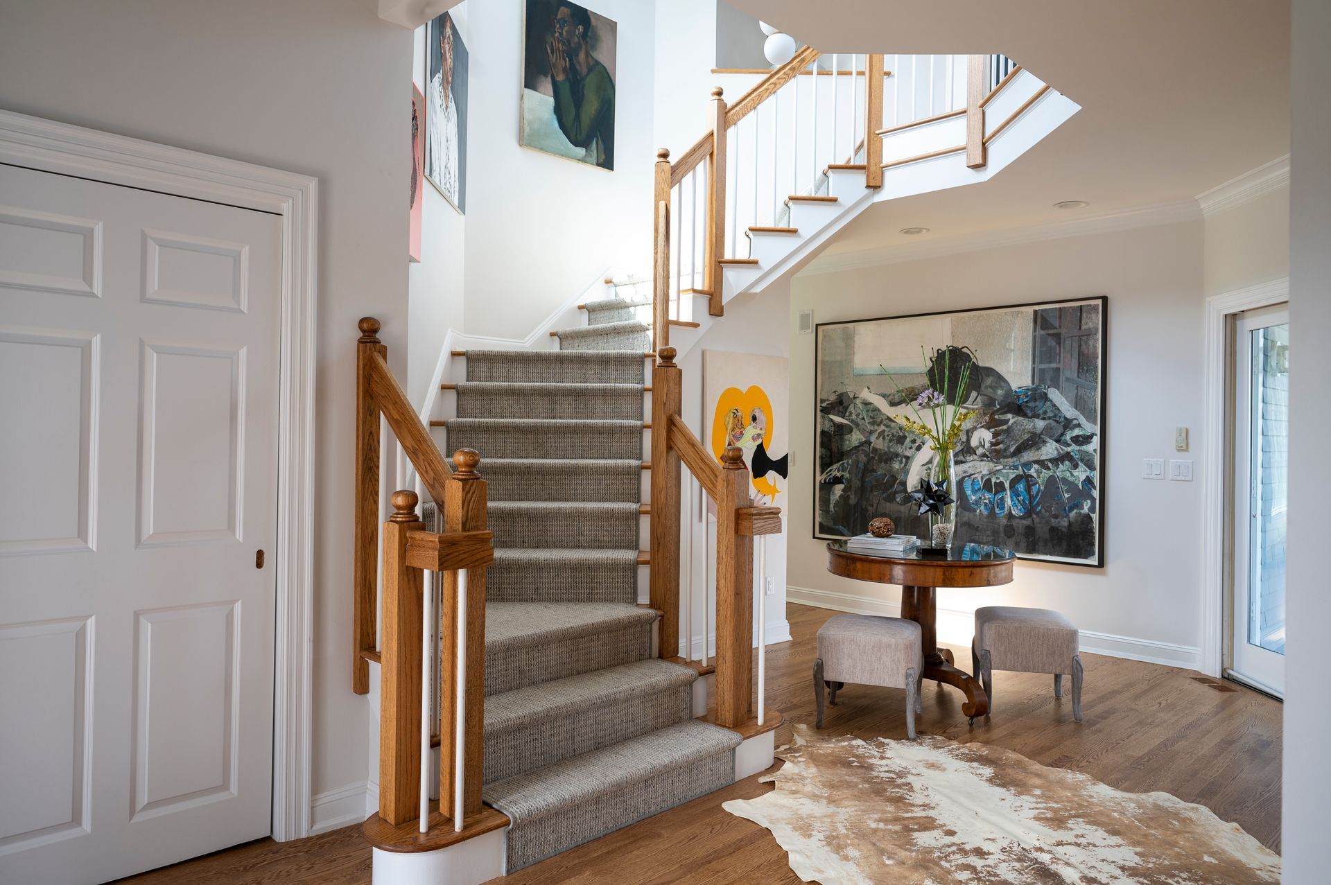 Bright foyer with curved staircase, carpeted steps, wood railings, and framed artwork on the wall.