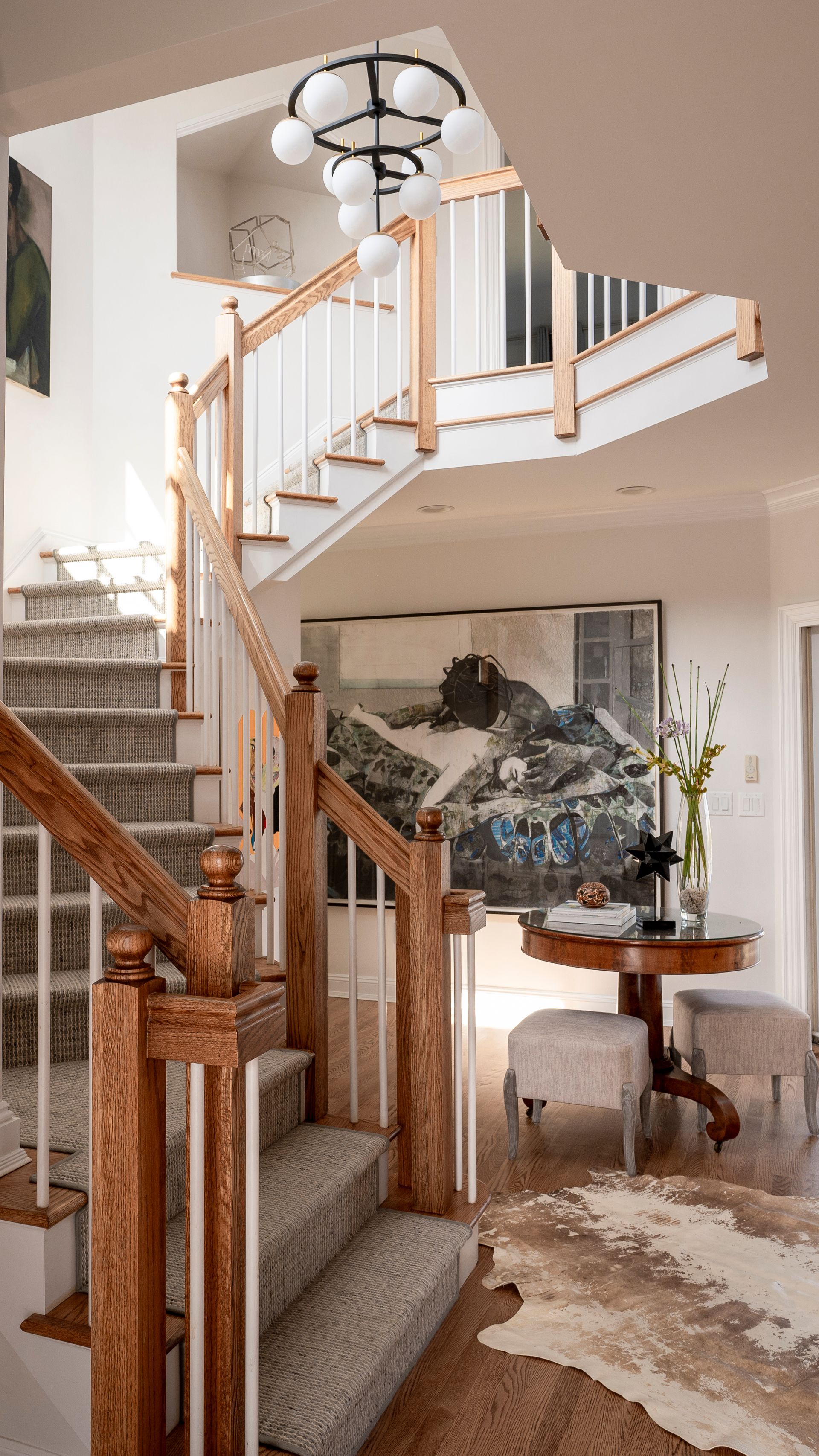 Curved staircase with wood railings and carpet in a bright foyer, with chandelier and floral wall art.