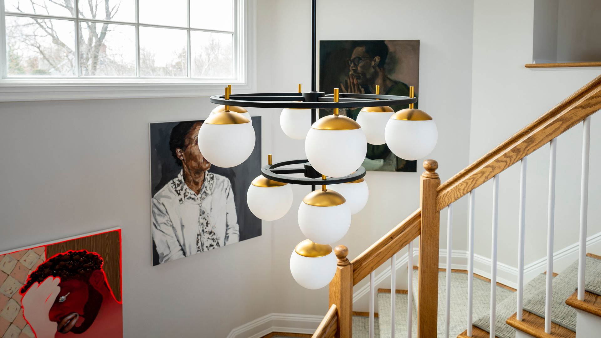 Staircase with gold railing and modern chandelier beside framed artwork and a window
