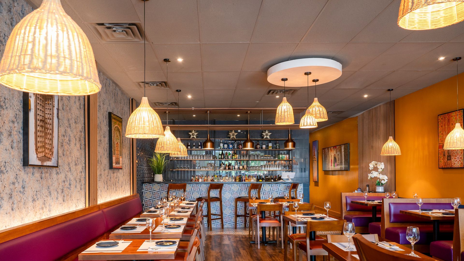 Cozy restaurant dining room with warm pendant lights, booths, tables, and a blue backlit bar.