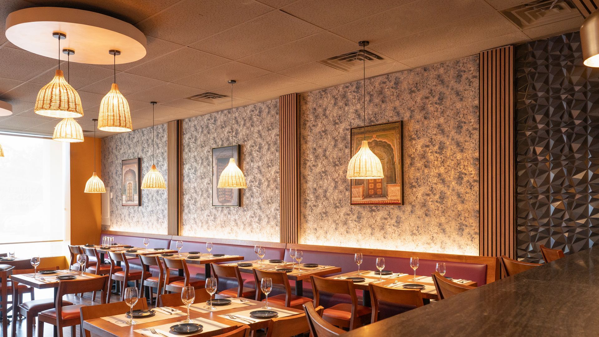 Empty restaurant dining area with warm pendant lights, set tables, and patterned wallpaper