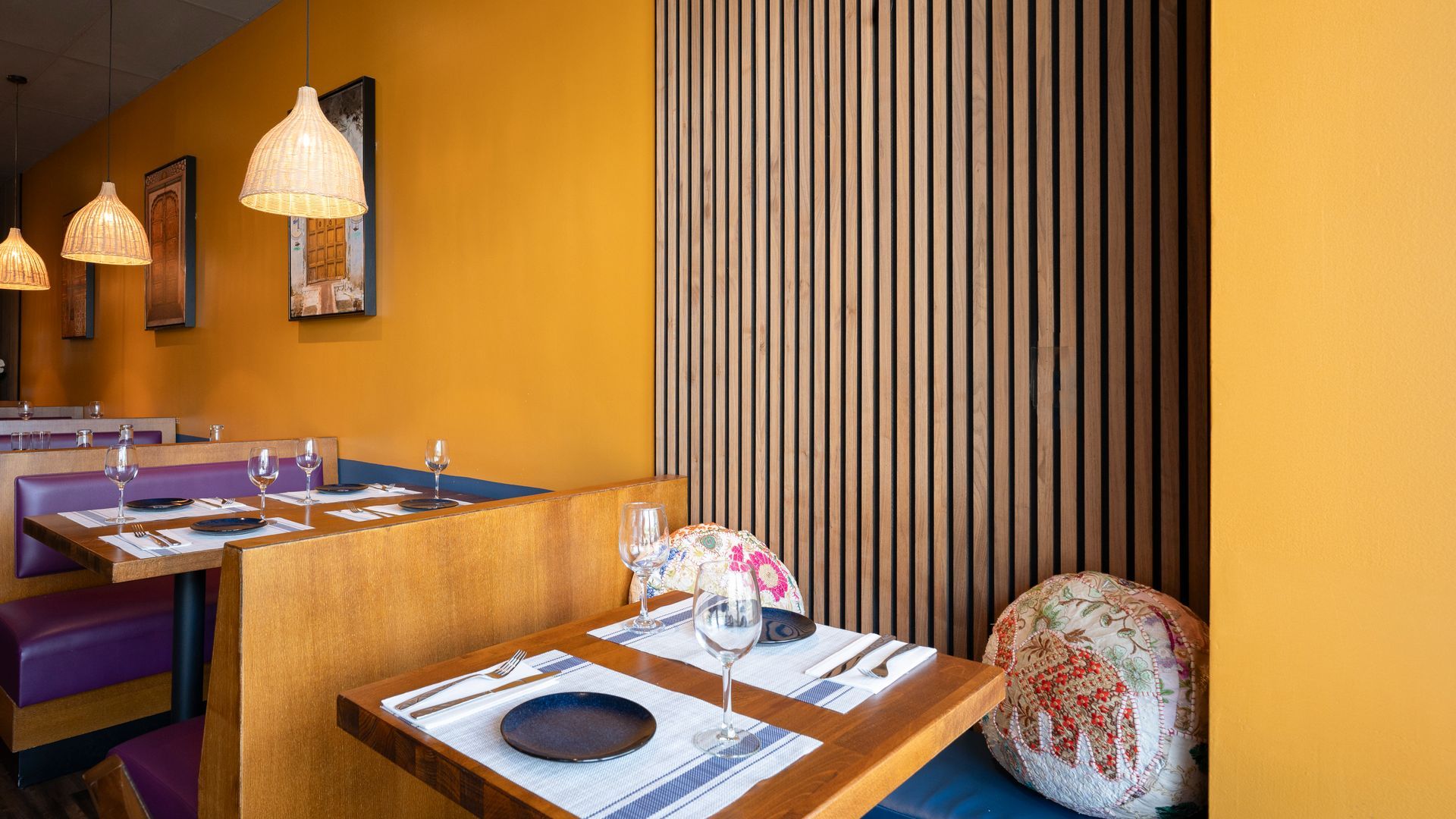Cozy restaurant booth with yellow walls, wooden dividers, hanging lamps, and neatly set tables.