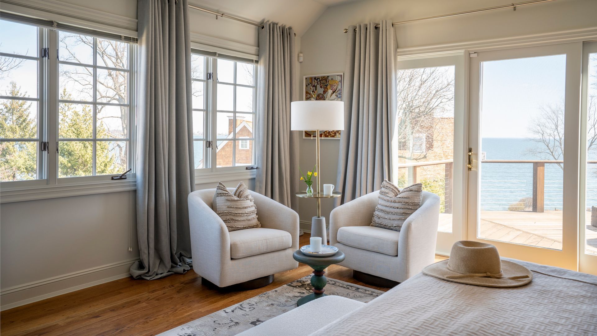 Bright bedroom with two armchairs by large windows and a view of the water