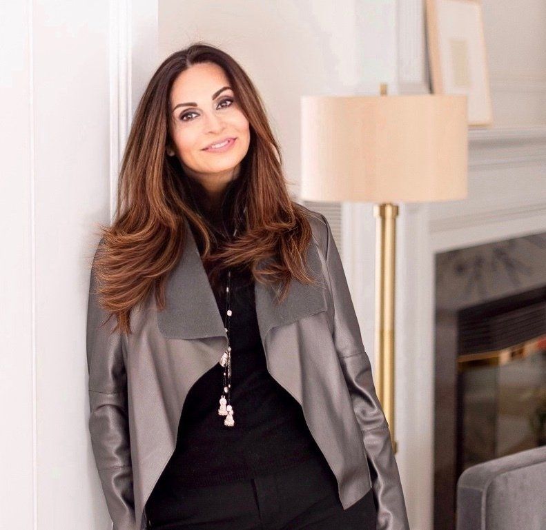 Woman in a gray jacket smiling in a modern living room beside a fireplace
