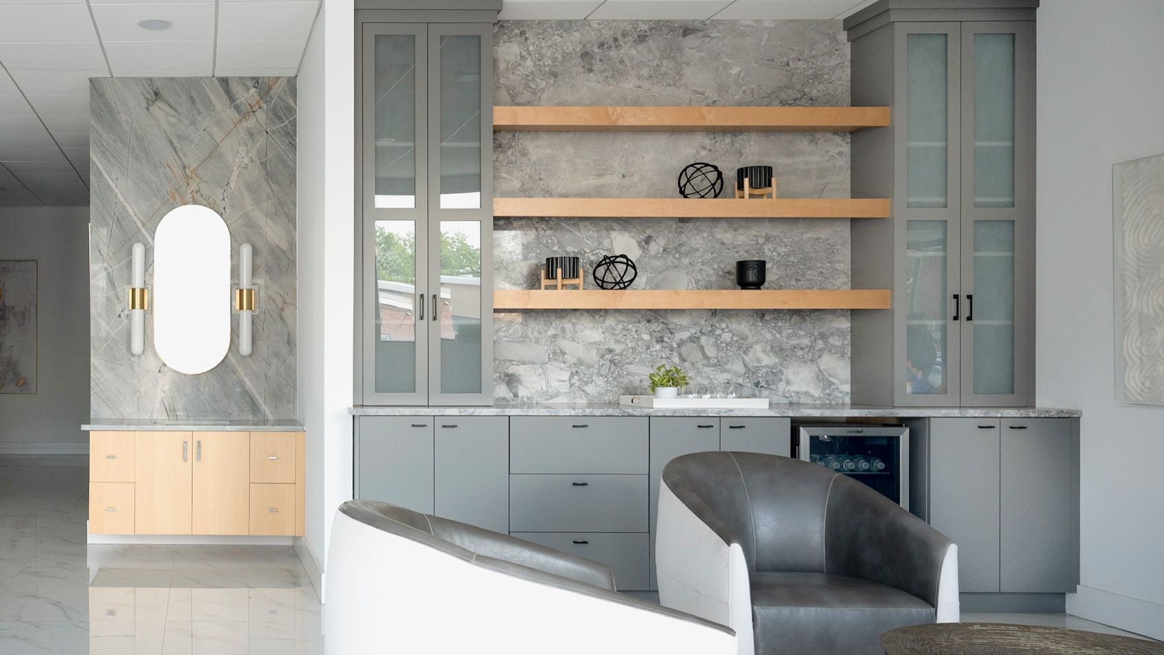 Modern gray kitchen with marble walls, open wood shelves, and a white island with a dark chair.