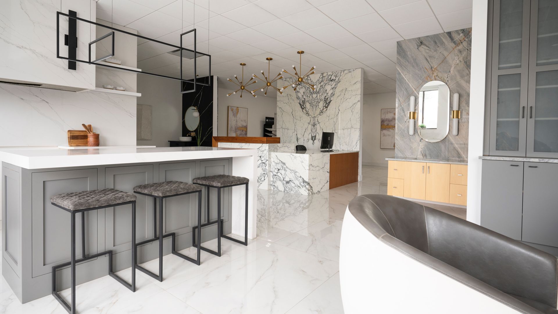 Modern white kitchen with island seating, pendant lights, and a round mirror in an adjoining entryway