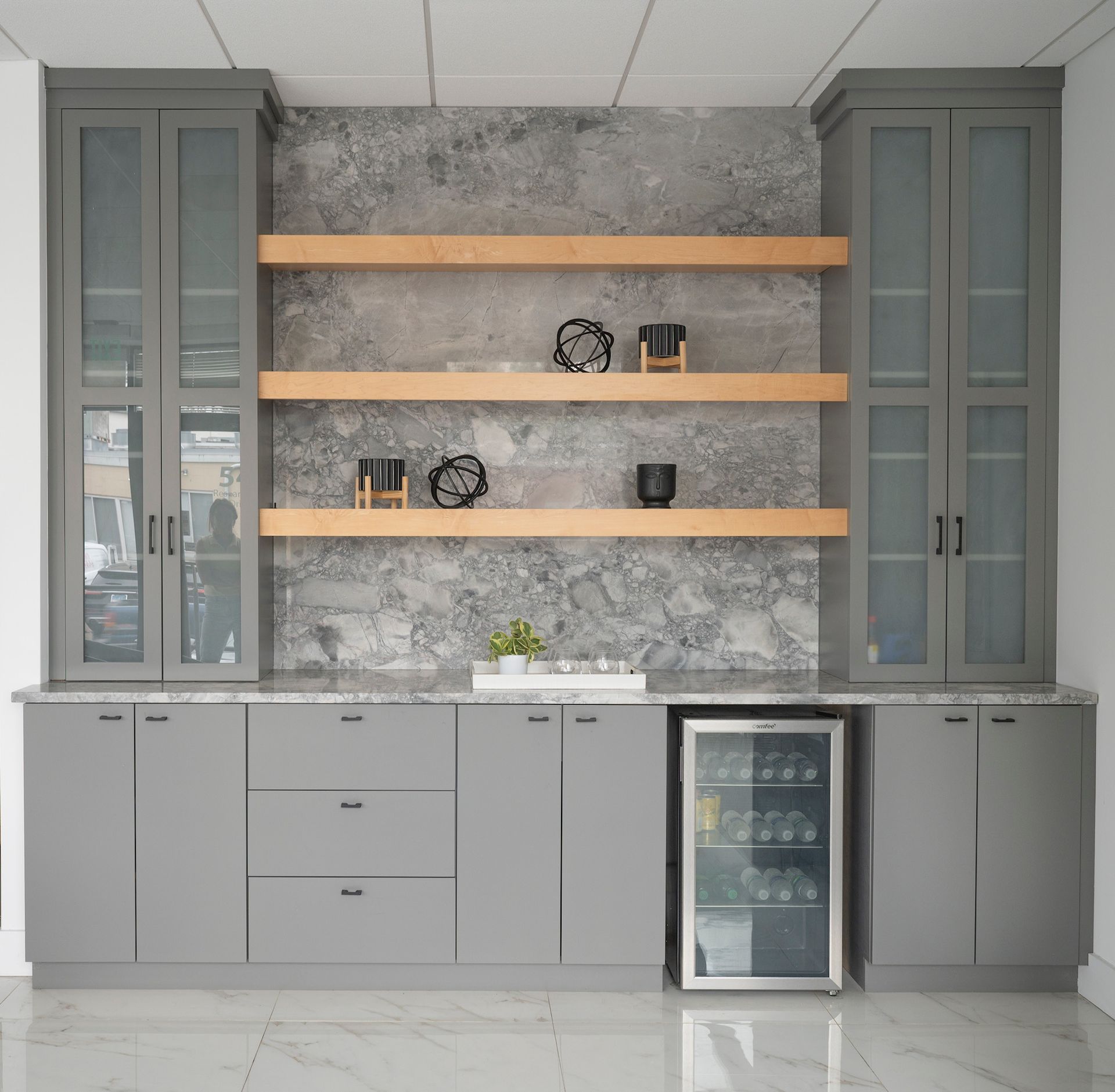 Modern built-in cabinetry with gray doors, wood shelves, and a marble floor in a minimalist room