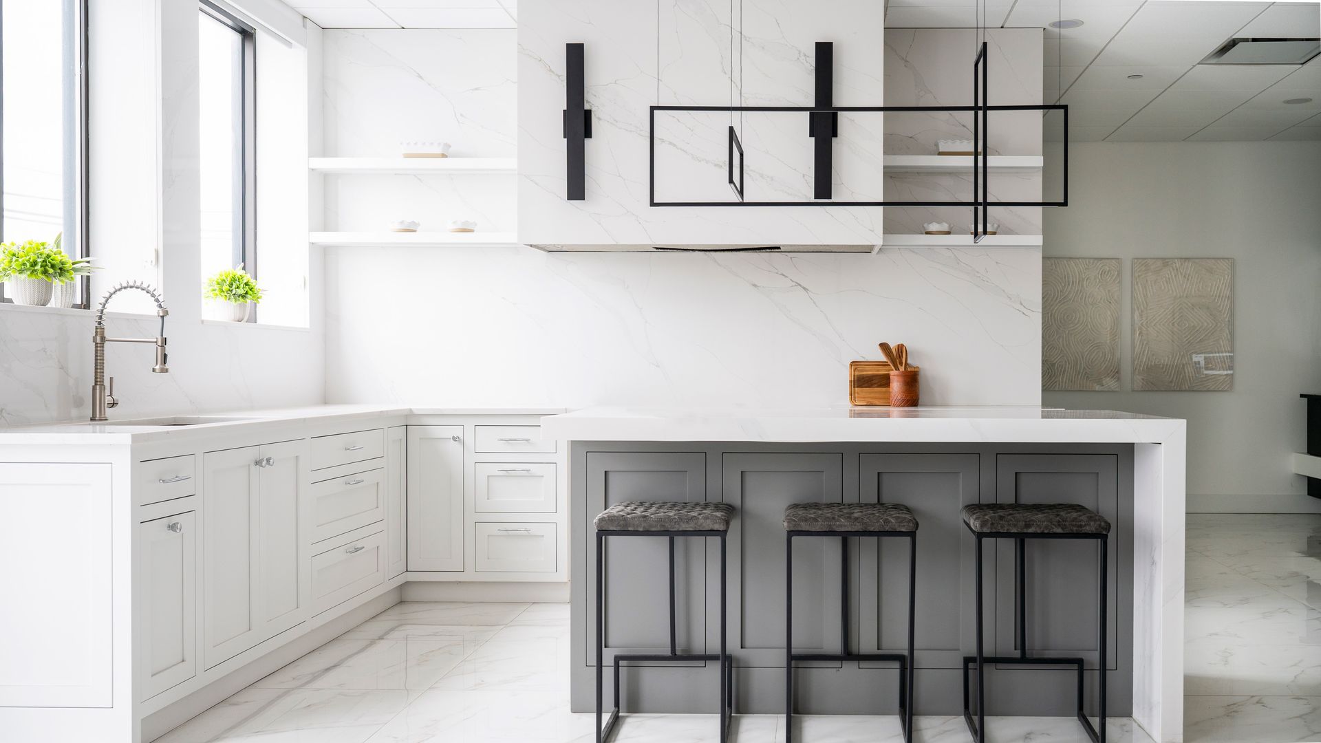 Bright modern white kitchen with island, black stools, and large windows by a sink