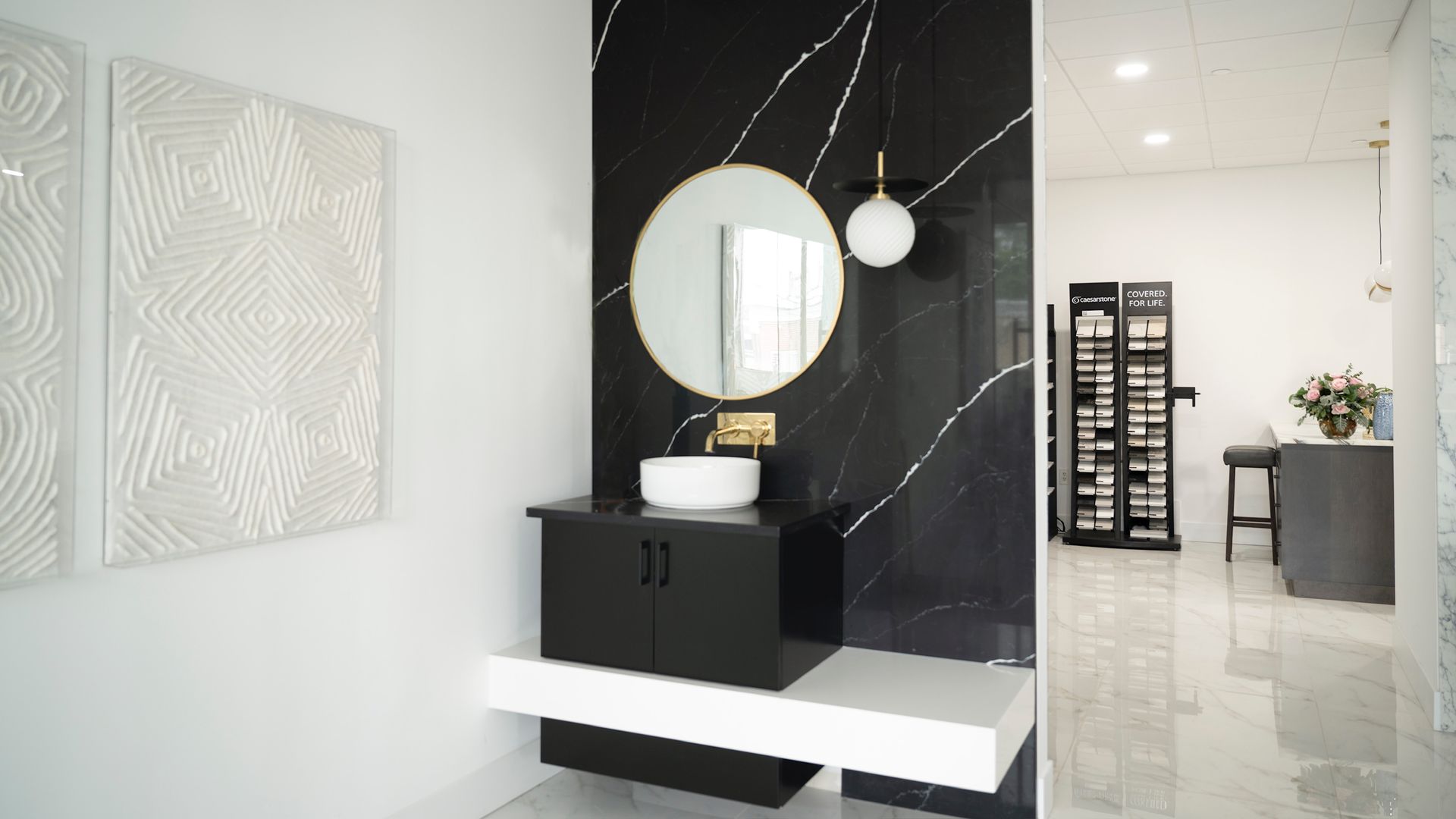 Modern lobby with black marble wall, round mirror, black bench, and bright white tiled floor.