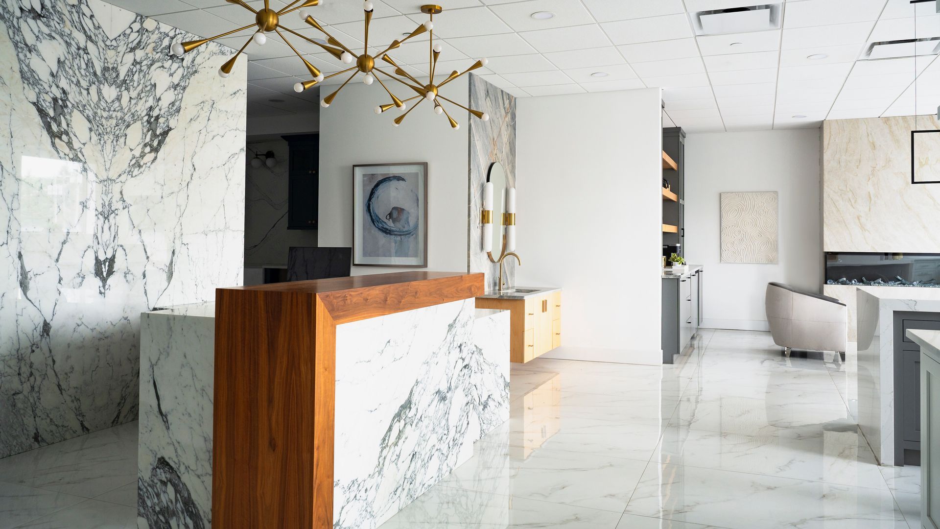 Modern marble lobby with a wooden reception desk, gold chandelier, and white seating area