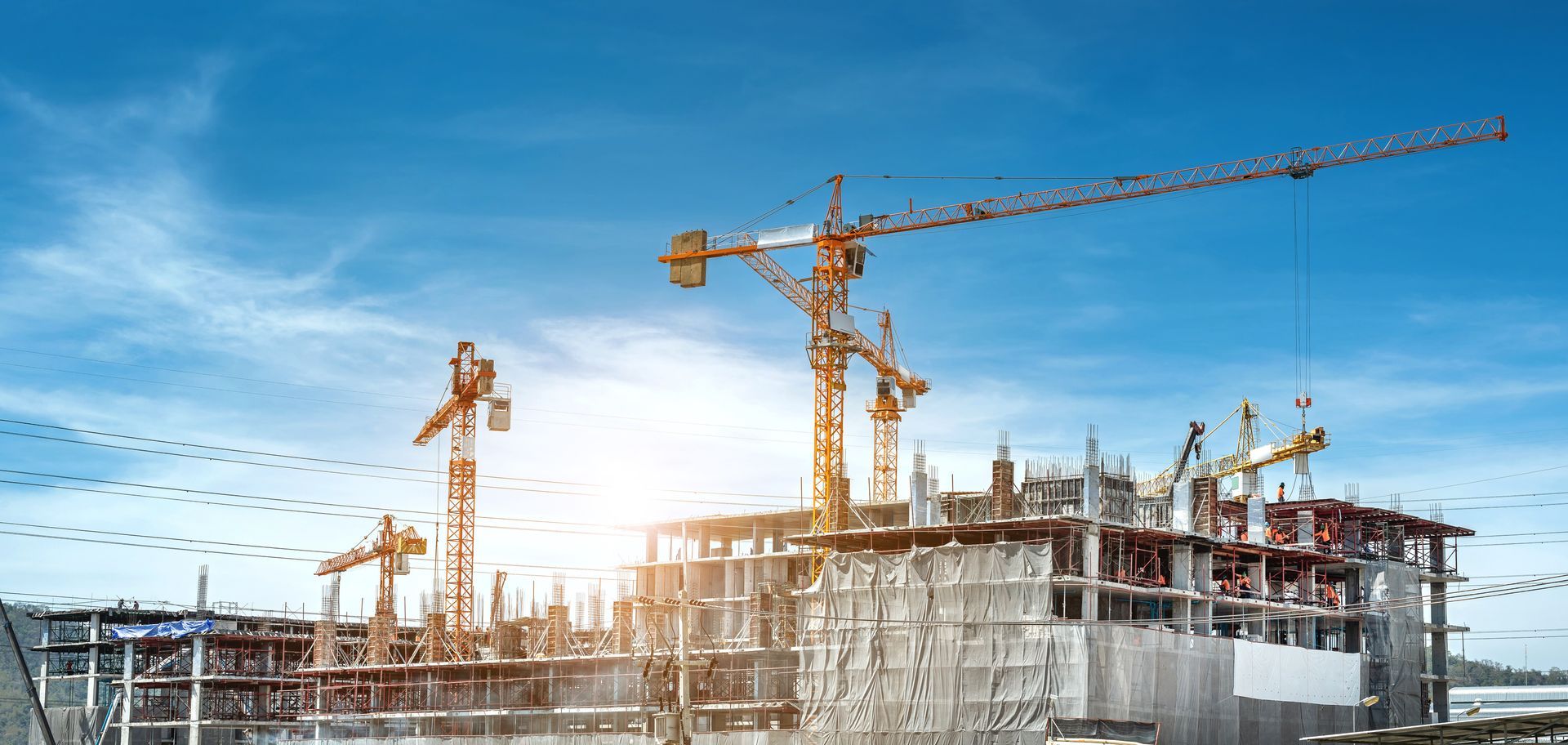Chantier de construction avec de multiples grues jaunes imposantes surplombant une grande structure de bâtiment sous un ciel d'un bleu éclatant.
