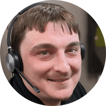 Man wearing a headset, smiling slightly, in a dimly lit setting.
