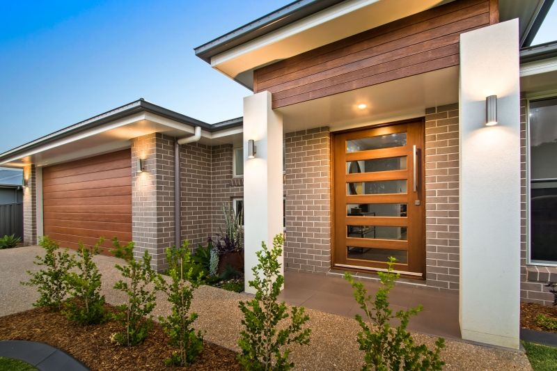 The front of a brick house with a wooden door. — Peter Betros Homes in Highfields, QLD