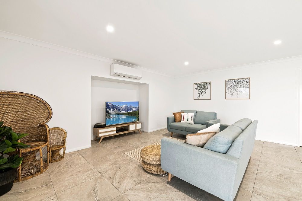 A living room with a couch , chair , table and television. — Peter Betros Homes in Highfields, QLD