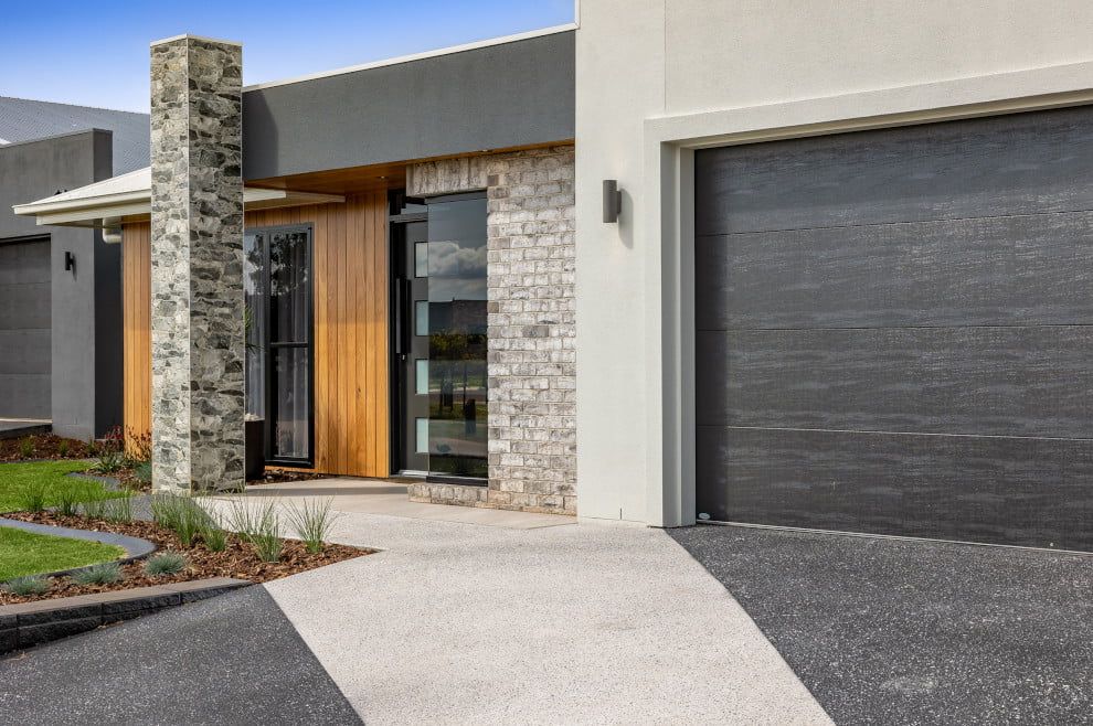 A Modern House with A Black Garage Door and A Stone Chimney — Peter Betros Homes in Highfields, QLD