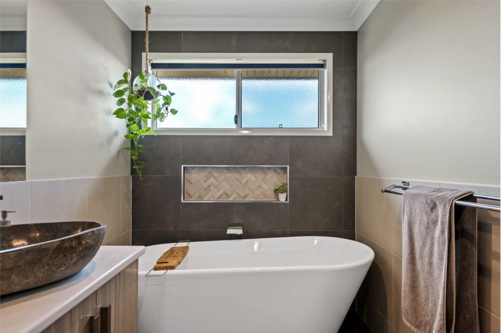 A bathroom with a tub , sink , mirror and window. — Peter Betros Homes in Highfields, QLD