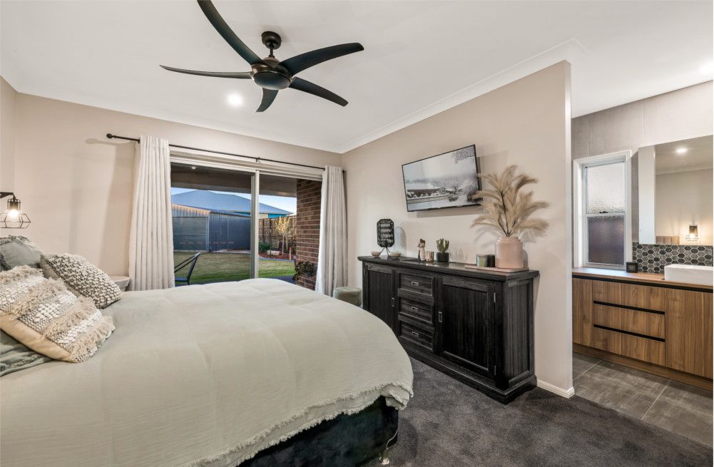A bedroom with a bed , dresser , television and ceiling fan. — Peter Betros Homes in Highfields, QLD