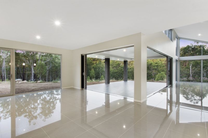 A large empty room with a lot of windows and a reflection of trees in the floor. — Peter Betros Homes in Highfields, QLD
